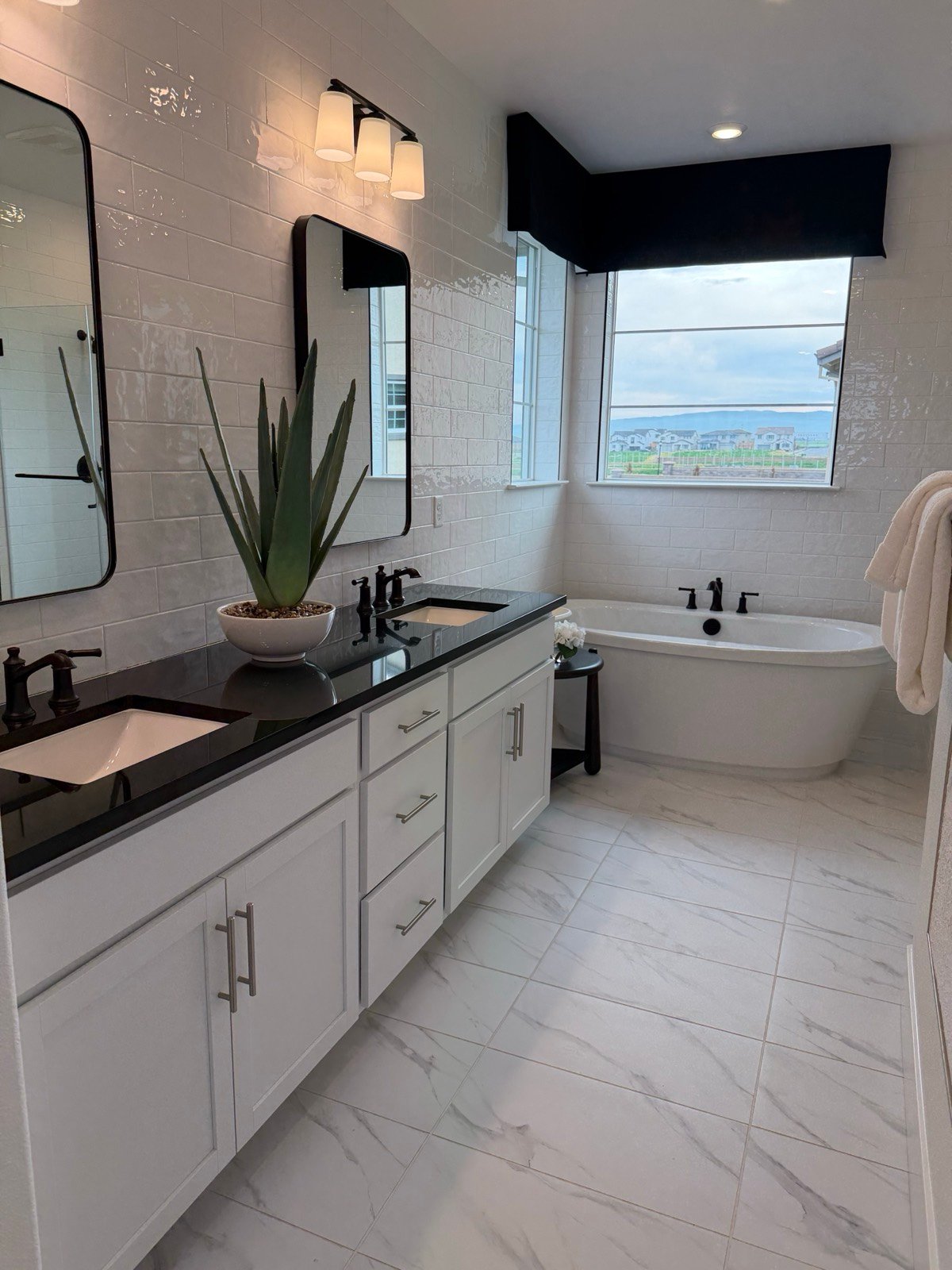 Bathroom with subway tile walls, dark double vanity with stone countertop, marble-look floor tile, and a freestanding tub