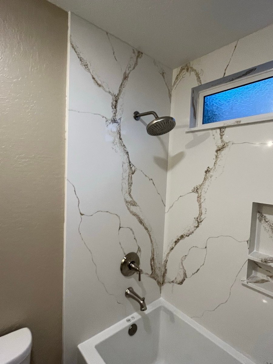 Close-up of shower fixtures against marble-look slab walls