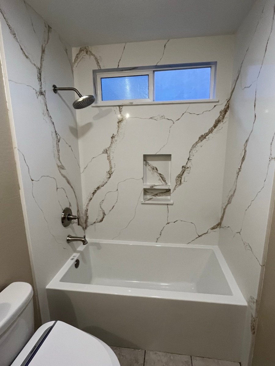 Marble-look shower with a niche and a window above the fixtures