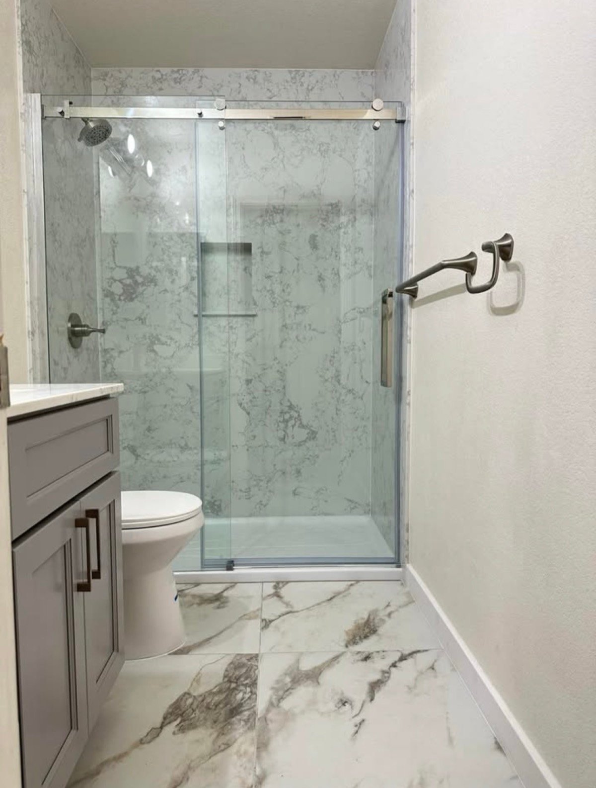 Bathroom shower and floor with large-format marble-look tile and a glass sliding door