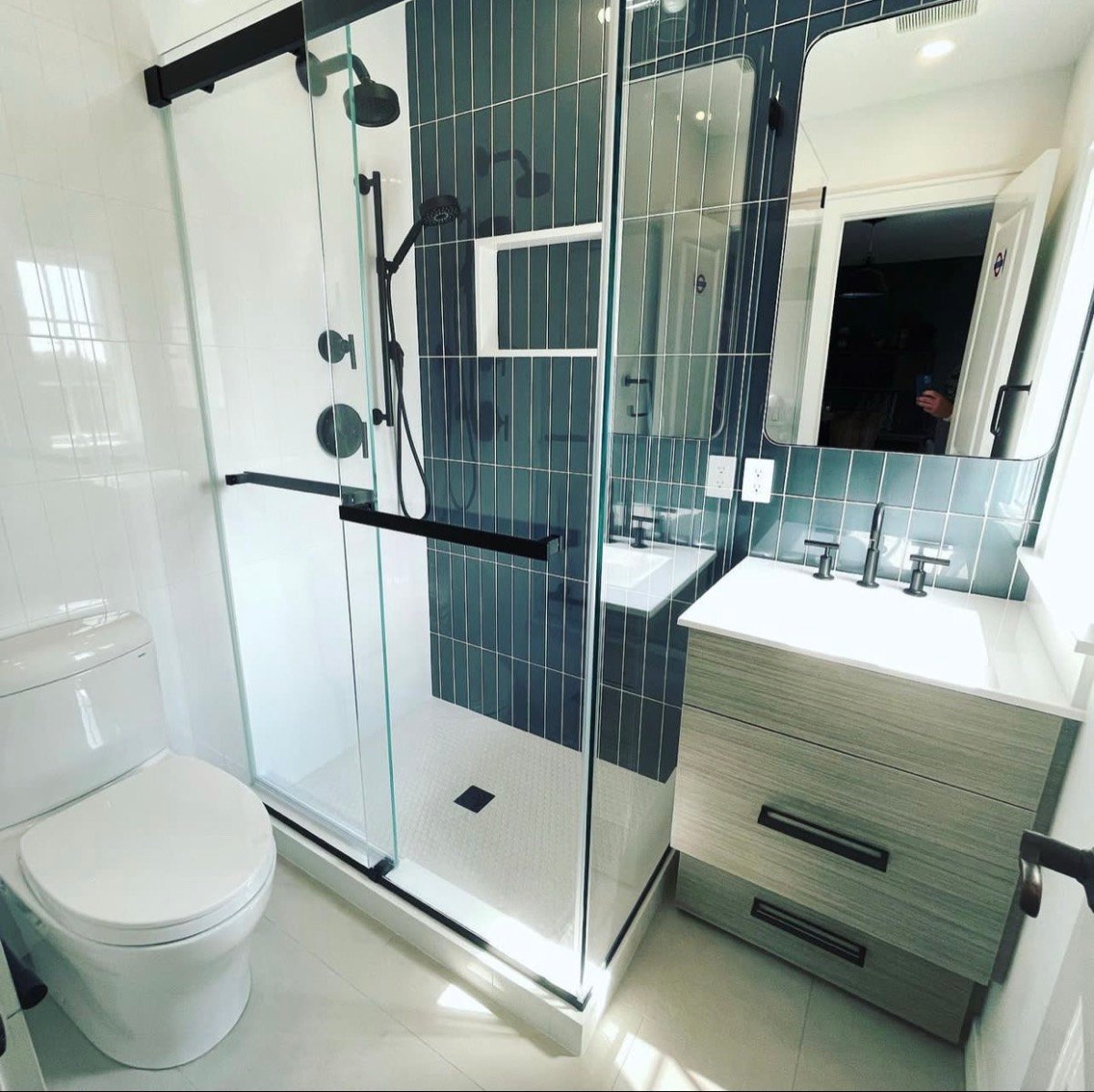 Modern glass shower with navy vertical tile, a floating vanity, and matte black fixtures