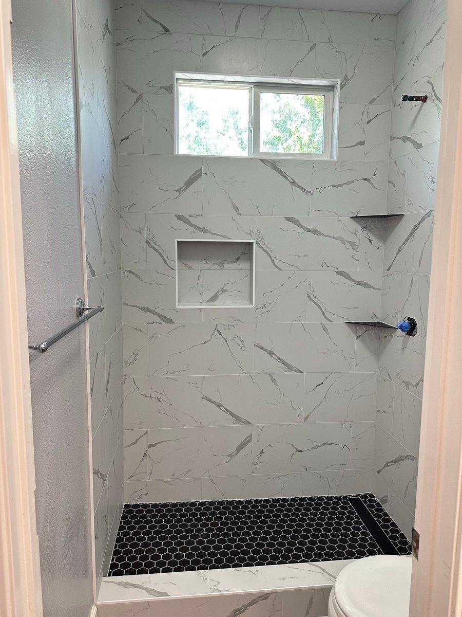 Marble-look shower tile with a niche and black hexagon mosaic accent