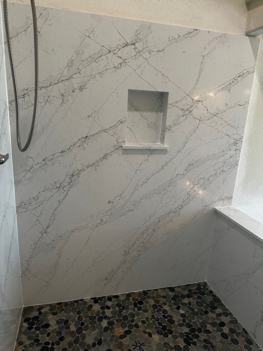 Shower corner with marble-look slab walls and a dark pebble mosaic accent wall