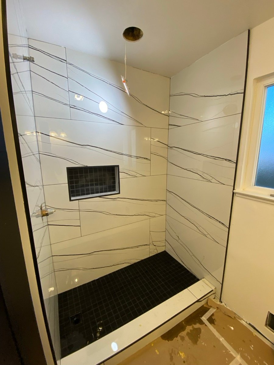 Marble-look large-format shower tile installation with a mosaic niche and floor