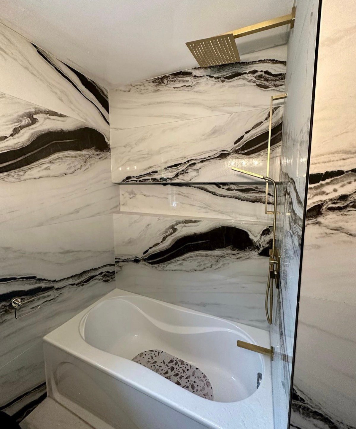 Soaking tub and shower with black-veined white marble slab walls and brushed brass fixtures