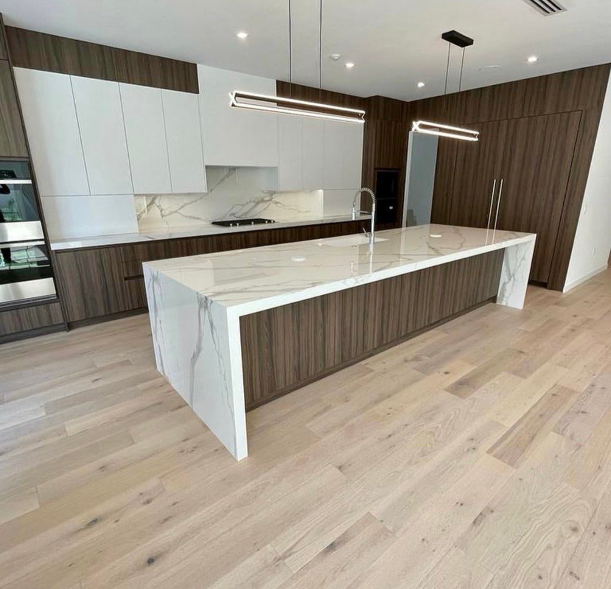 Modern kitchen with dark wood cabinetry, a marble-look waterfall island, and linear pendant lighting