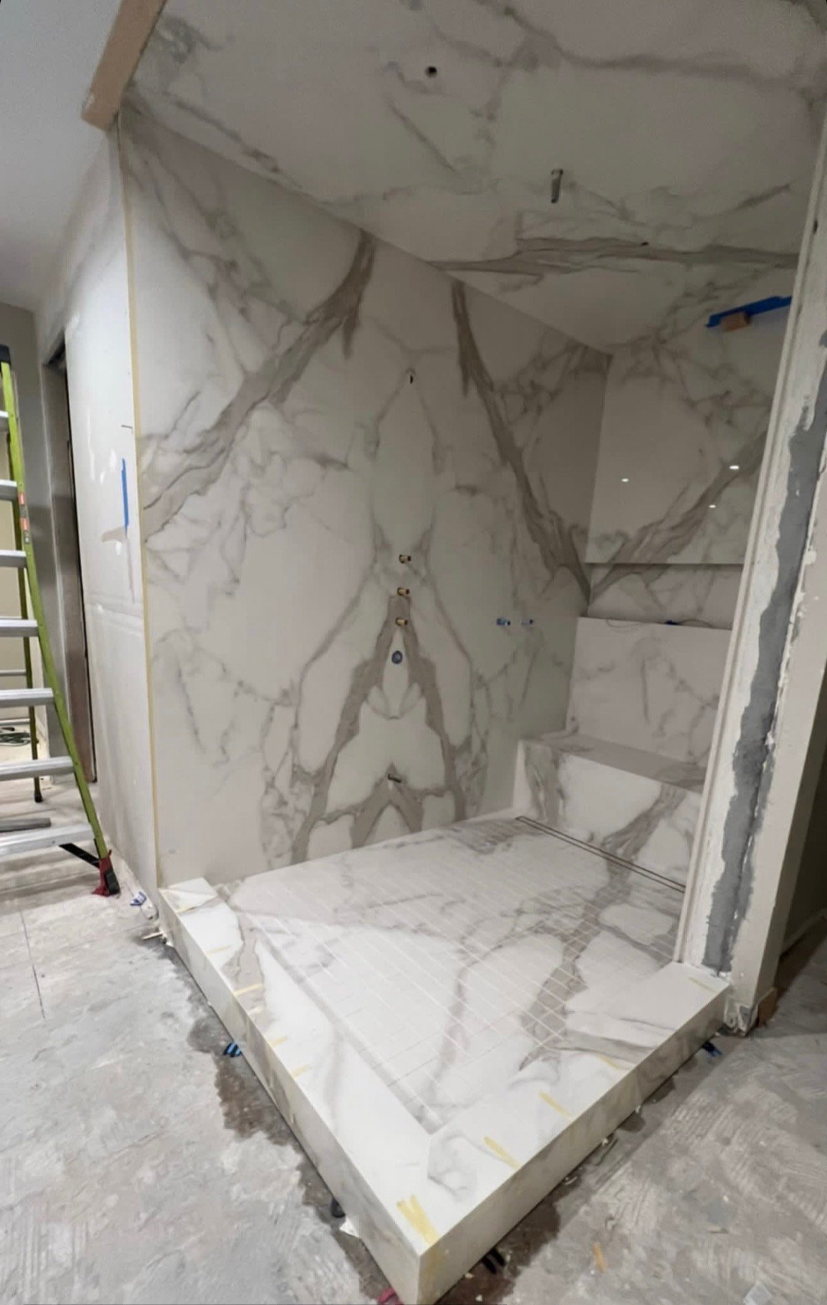 Shower with a built-in marble-look waterfall-edge bench and matching slab walls